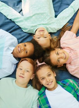 Top view at multi-ethnic group of kids lying in circle on blanket outdoors and looking at camera